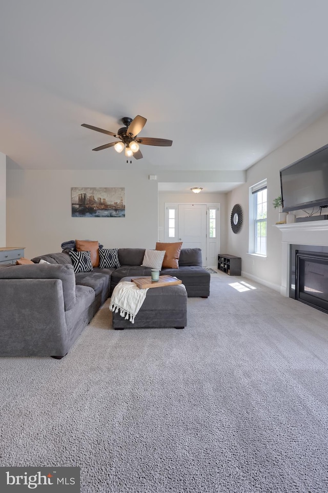 carpeted living room with a ceiling fan, a glass covered fireplace, and baseboards