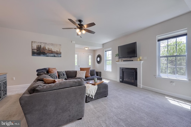 living room featuring carpet floors, baseboards, a ceiling fan, and a glass covered fireplace