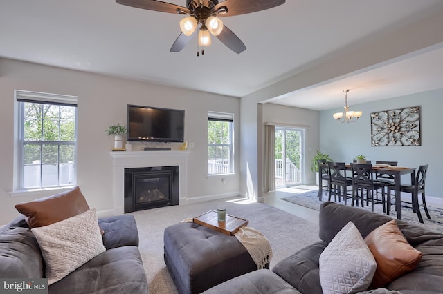 living room featuring baseboards, a chandelier, a glass covered fireplace, carpet flooring, and a ceiling fan