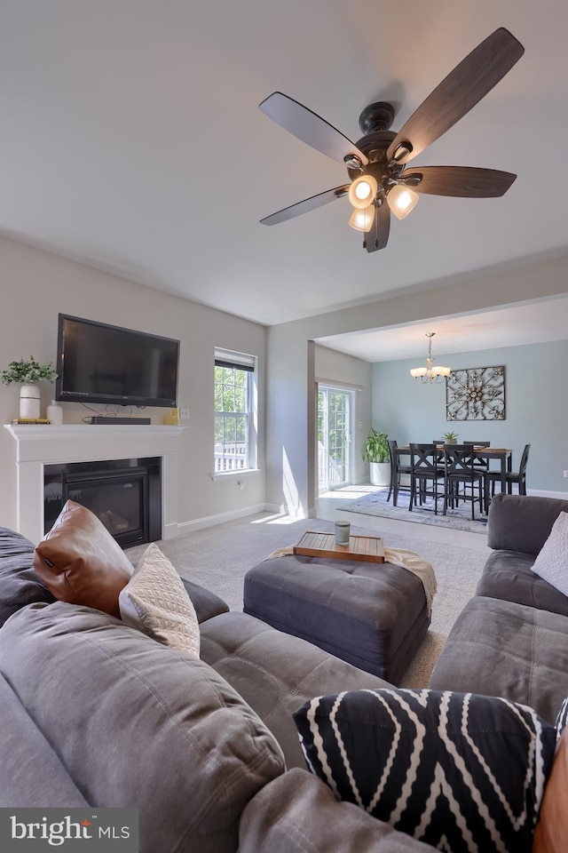 living room with carpet flooring, a ceiling fan, a chandelier, a glass covered fireplace, and baseboards