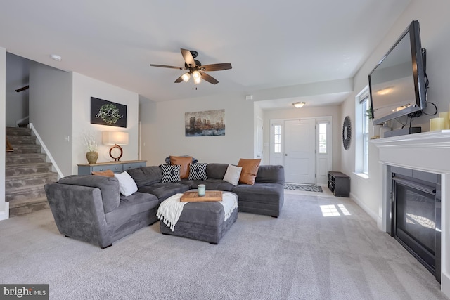 carpeted living room with stairway, ceiling fan, baseboards, and a glass covered fireplace