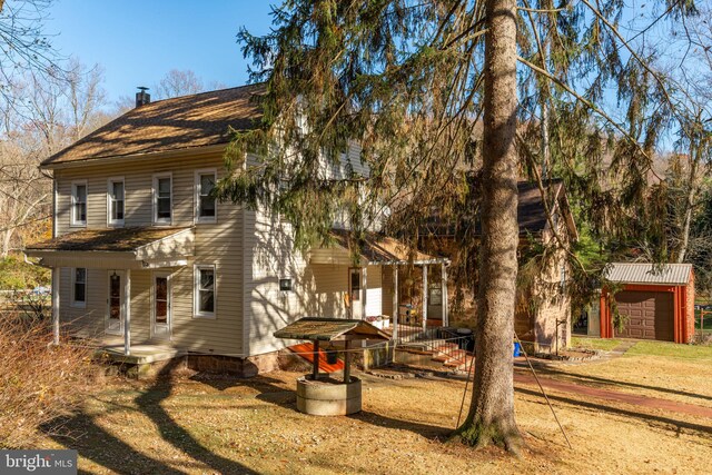 view of front facade featuring covered porch, a chimney, an outdoor structure, and a front lawn