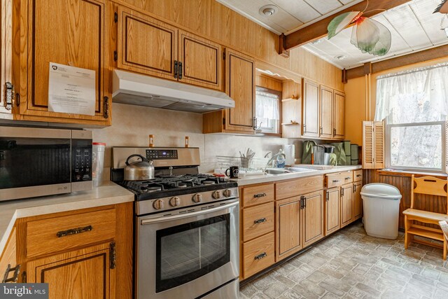 kitchen with under cabinet range hood, stainless steel appliances, light countertops, a sink, and brown cabinetry