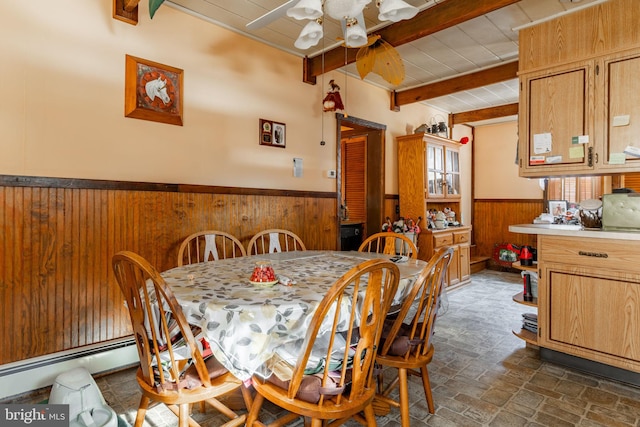 dining room with a wainscoted wall, wood walls, beam ceiling, a ceiling fan, and brick patterned floors
