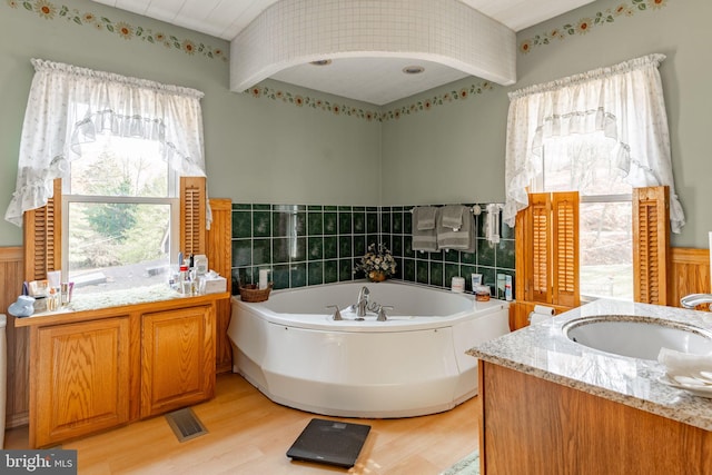 full bath with wood finished floors, a wainscoted wall, a bath, and vanity