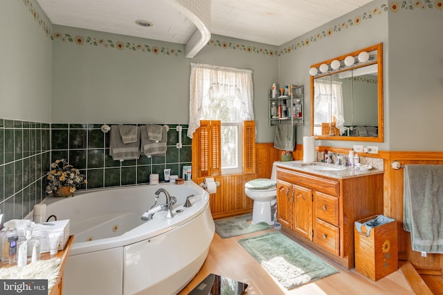 bathroom featuring a wainscoted wall, wood finished floors, a whirlpool tub, vanity, and toilet