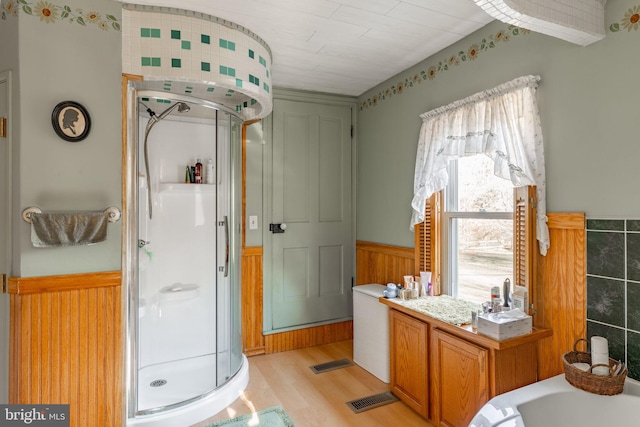 full bathroom featuring a shower stall, wainscoting, and wood finished floors