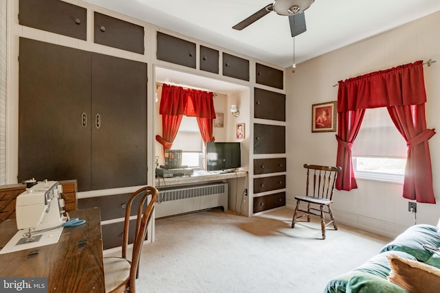 living area with carpet flooring, a ceiling fan, a desk, and radiator heating unit