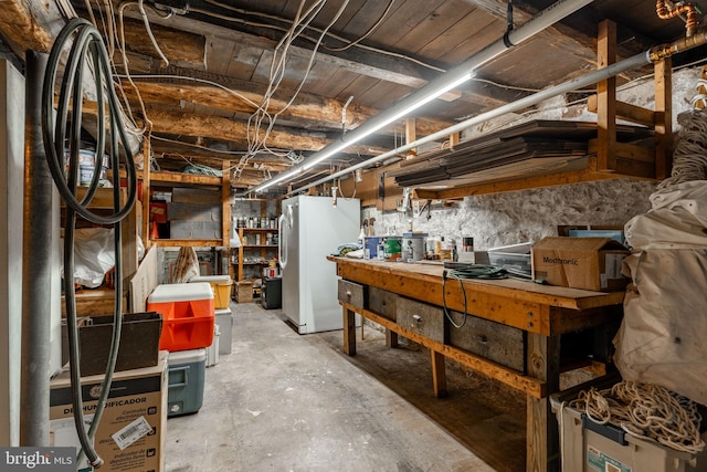 unfinished below grade area featuring freestanding refrigerator and a workshop area