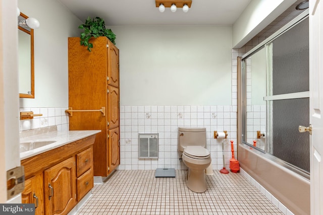 full bath with tile walls, heating unit, combined bath / shower with glass door, toilet, and vanity
