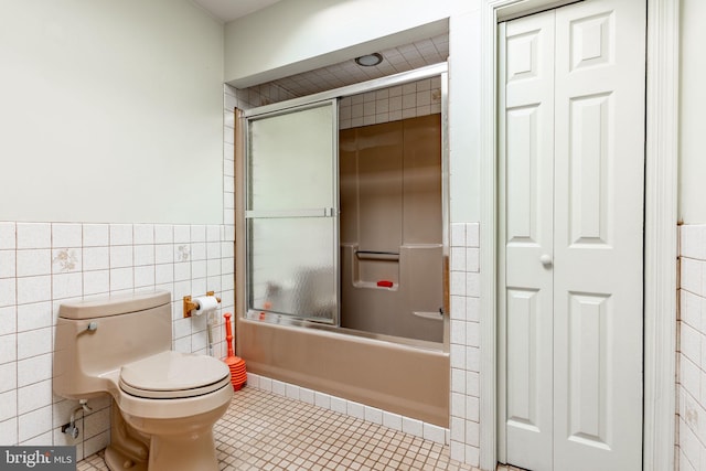bathroom with tile walls, a closet, enclosed tub / shower combo, toilet, and tile patterned flooring