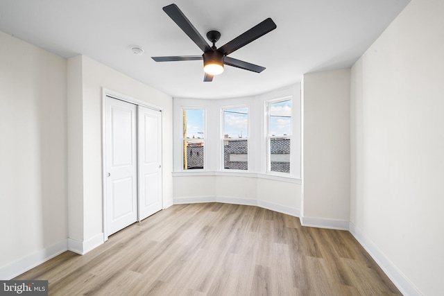 unfurnished bedroom with wood finished floors, baseboards, a closet, and a ceiling fan