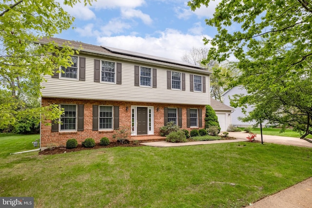 colonial-style house with roof mounted solar panels, a front lawn, brick siding, concrete driveway, and an attached garage