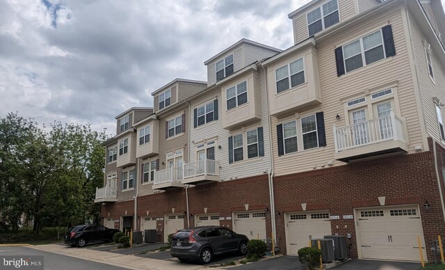 view of building exterior with an attached garage, driveway, and central AC