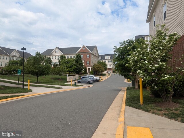 view of asphalt road with sidewalks, a residential view, curbs, and street lights