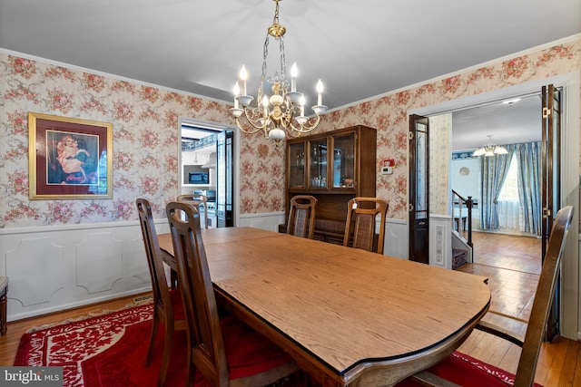 dining room with a chandelier, healthy amount of natural light, a wainscoted wall, wallpapered walls, and hardwood / wood-style floors