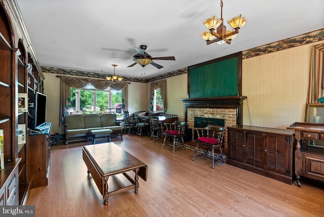 living area featuring wallpapered walls, wood finished floors, ceiling fan, a brick fireplace, and a chandelier