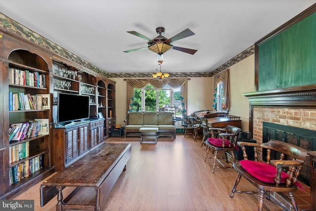 living room with a ceiling fan, wood finished floors, wallpapered walls, and a brick fireplace