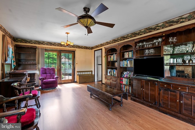 living room featuring wood finished floors, a chandelier, a ceiling fan, and wallpapered walls