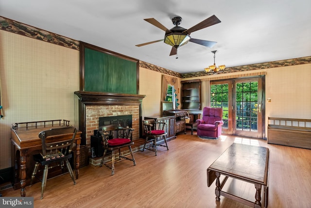 living room featuring wallpapered walls, wood finished floors, a fireplace, and a ceiling fan
