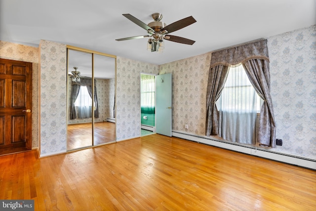 unfurnished bedroom with a baseboard radiator, wood finished floors, wallpapered walls, and a closet