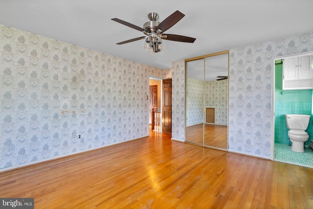 unfurnished bedroom featuring hardwood / wood-style floors, a closet, baseboards, wallpapered walls, and connected bathroom