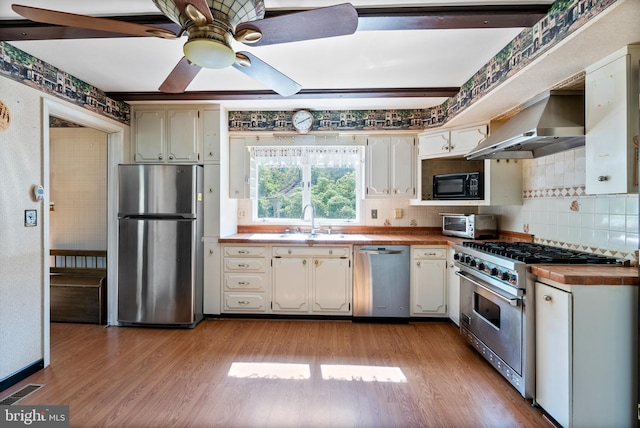 kitchen featuring appliances with stainless steel finishes, wall chimney exhaust hood, a sink, tasteful backsplash, and wood finished floors