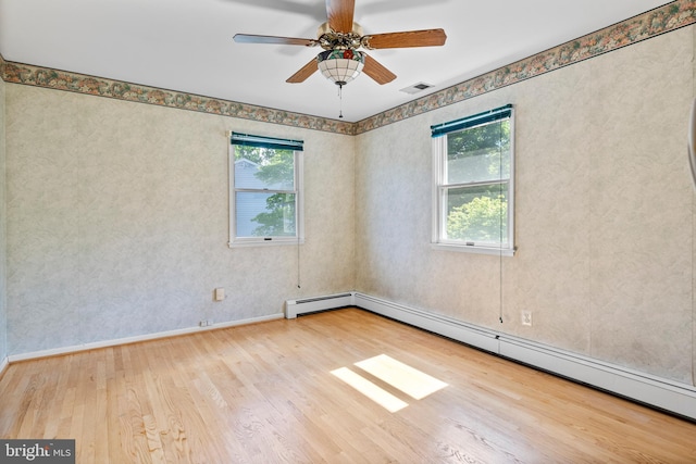 spare room featuring wood finished floors, a baseboard heating unit, ceiling fan, and baseboards