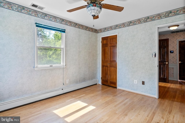 empty room featuring baseboard heating, wood finished floors, ceiling fan, and wallpapered walls