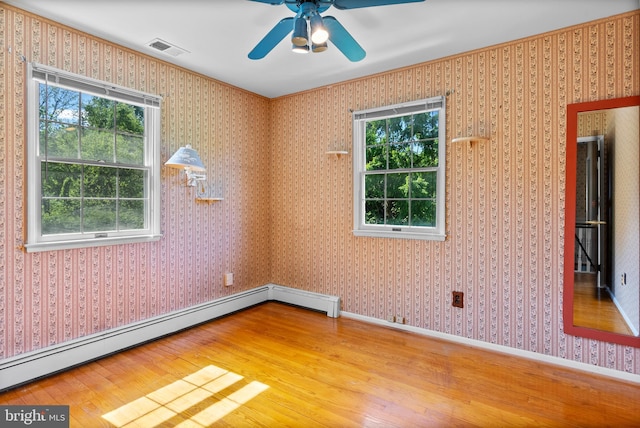 empty room featuring a baseboard heating unit, wood finished floors, healthy amount of natural light, and ceiling fan