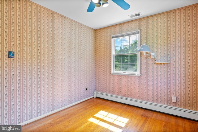 spare room featuring wood-type flooring, a baseboard radiator, a ceiling fan, ornamental molding, and baseboards