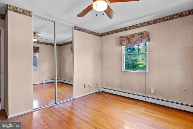 unfurnished bedroom with a baseboard radiator, wood finished floors, a closet, ceiling fan, and baseboards