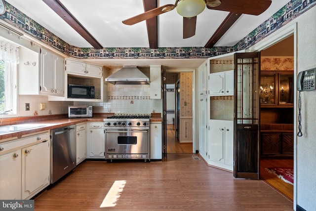 kitchen with stainless steel appliances, wall chimney exhaust hood, backsplash, dark wood-type flooring, and wallpapered walls