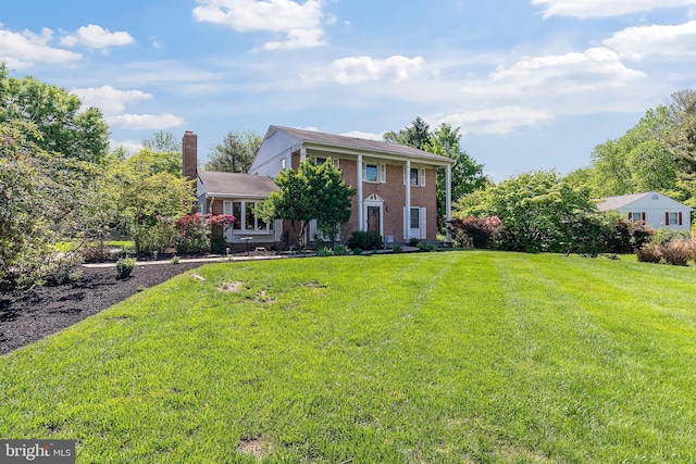 greek revival house with brick siding, a front lawn, and a chimney