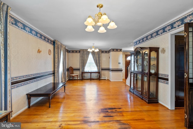 dining room featuring a chandelier, wallpapered walls, wood finished floors, baseboards, and ornamental molding