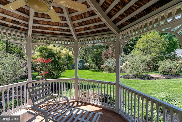 wooden terrace with a gazebo, a lawn, a storage unit, an outbuilding, and ceiling fan