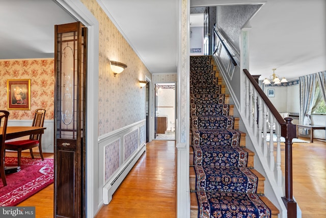 stairs with wallpapered walls, a baseboard heating unit, a chandelier, a wainscoted wall, and wood finished floors