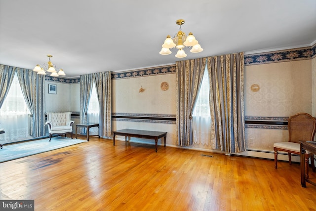 living area featuring a chandelier, wallpapered walls, wood finished floors, a baseboard radiator, and crown molding