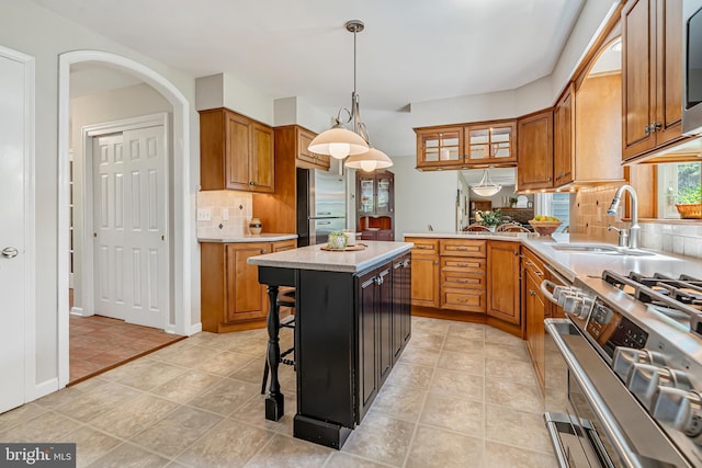 kitchen featuring stainless steel appliances, a sink, brown cabinetry, tasteful backsplash, and pendant lighting