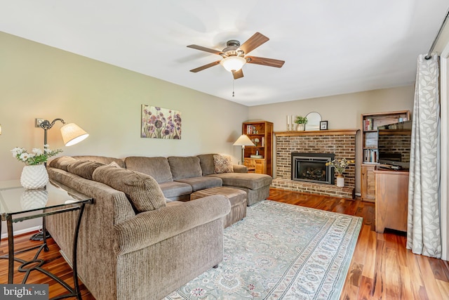 living area with ceiling fan, a brick fireplace, and wood finished floors
