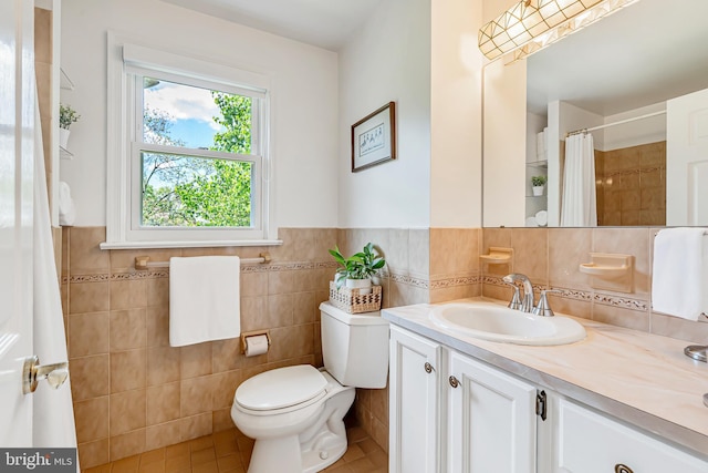 full bath with tile walls, tile patterned flooring, vanity, toilet, and wainscoting