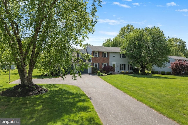 colonial-style house featuring a front lawn, driveway, brick siding, and a garage