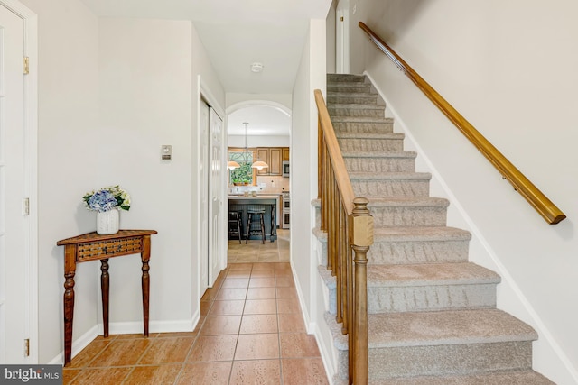 staircase featuring arched walkways, tile patterned flooring, and baseboards