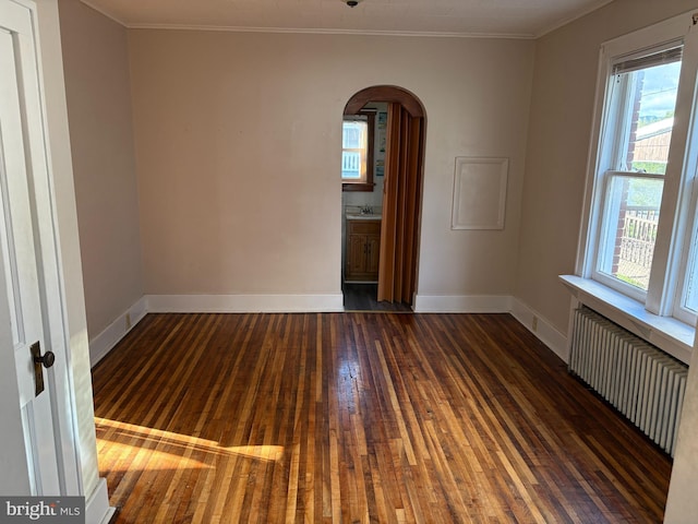 unfurnished room with radiator, arched walkways, ornamental molding, hardwood / wood-style floors, and baseboards