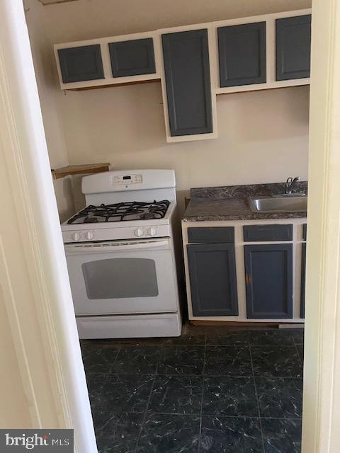 kitchen with white gas stove, a sink, gray cabinetry, and dark countertops