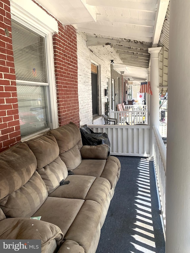 carpeted living room with brick wall and beamed ceiling