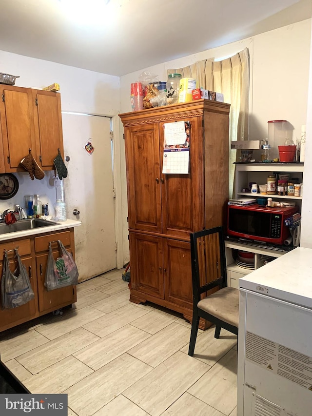 kitchen featuring light countertops, brown cabinets, a sink, and light wood finished floors