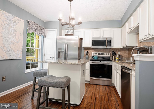 kitchen featuring appliances with stainless steel finishes, a kitchen island, tasteful backsplash, dark wood-type flooring, and white cabinets
