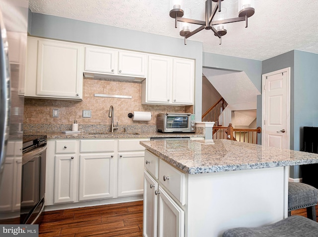 kitchen with a sink, dark wood-style flooring, stove, a chandelier, and decorative backsplash