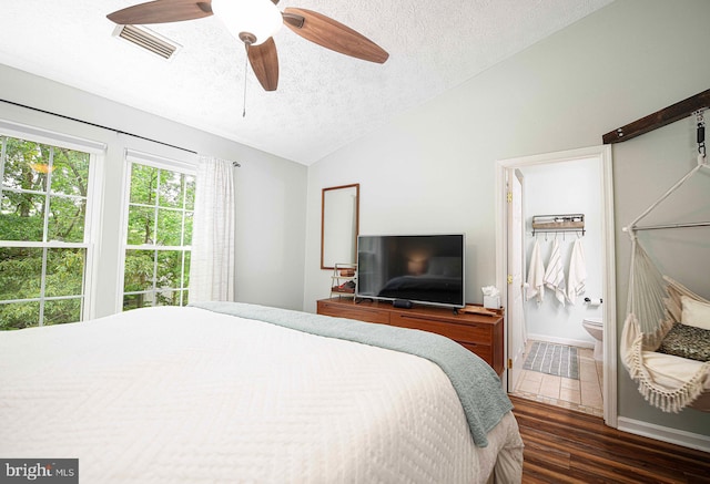 bedroom featuring lofted ceiling, a textured ceiling, dark wood finished floors, ensuite bath, and ceiling fan